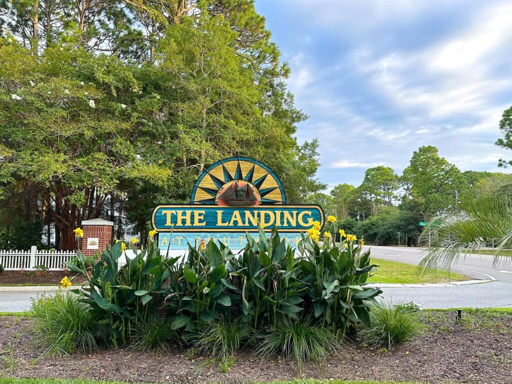 Entrance sign for The Landing community surrounded by green landscaping, trees, and yellow flowering plants.