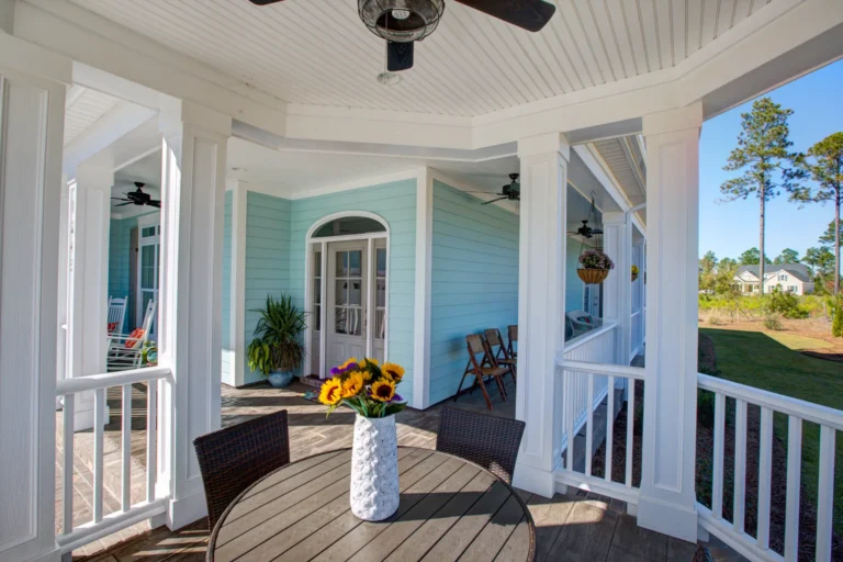 Coastal blue house porch with sunflowers, white trim, and wooden seating for relaxing outdoors.