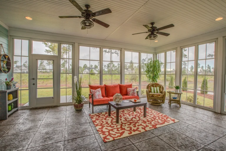Bright glass sunroom with red sofa, wicker chair, and garden views filled with natural light.
