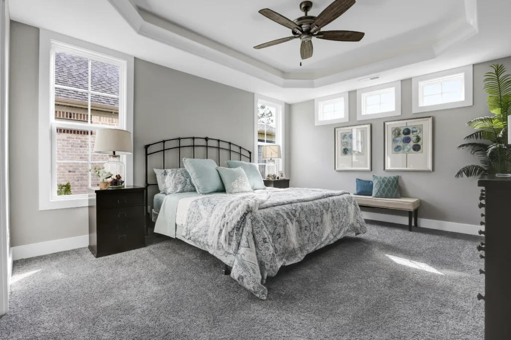 Elegant gray bedroom with tray ceiling, modern fan, patterned bedding, and calming neutral decor.