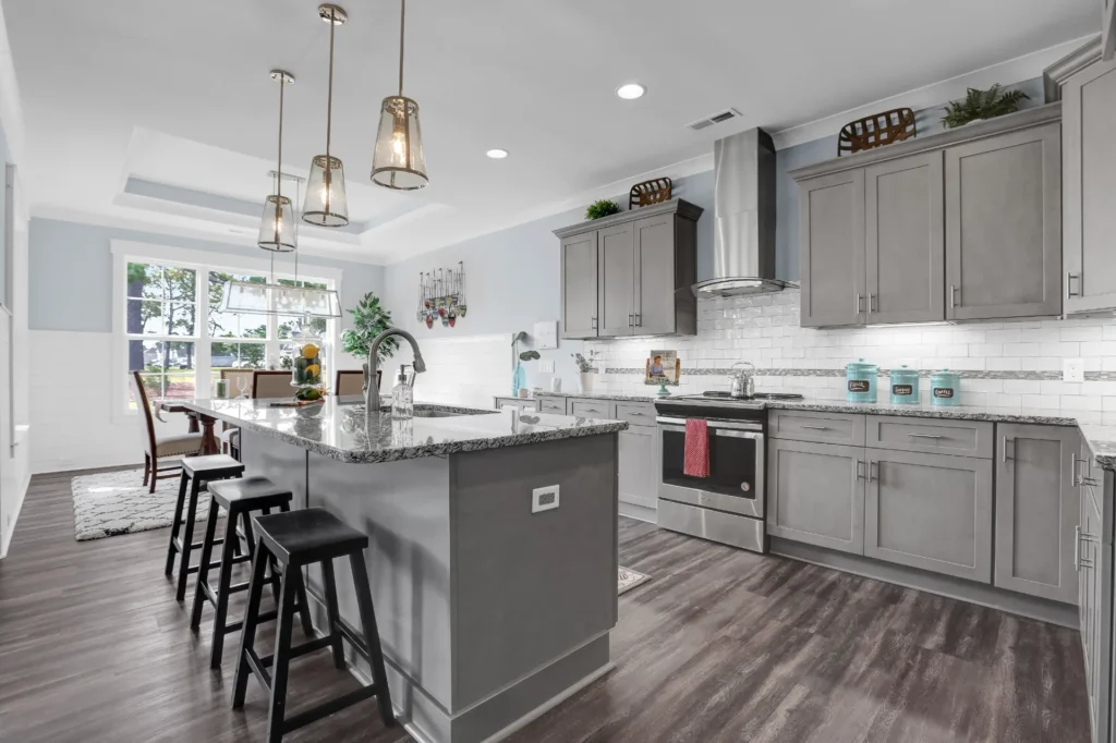 Modern gray kitchen with granite island, pendant lights, and stainless steel appliances.