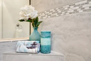 Calming bathroom decor with white flower, blue candle, and rolled towel on marble tile.