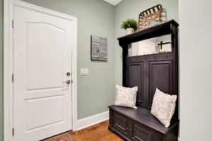 Cozy mudroom entryway with dark wooden hall tree, mirror, storage bench, and green accent wall.