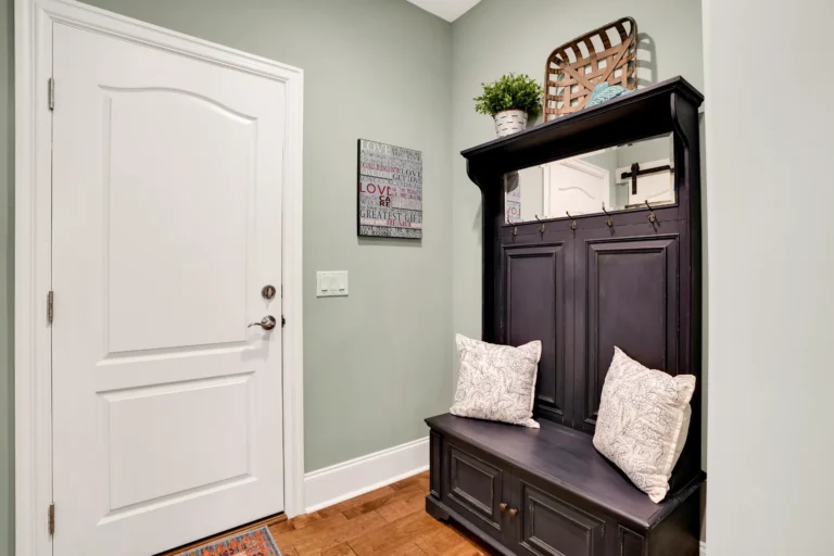 Cozy mudroom entryway with dark wooden hall tree, mirror, storage bench, and green accent wall.