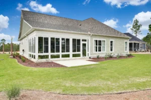 Modern beige suburban home with sunroom, gray roof, and landscaped backyard under blue sky