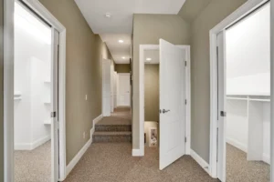 Modern hallway with beige walls, soft carpet, recessed lighting, and white trim creating a warm space.