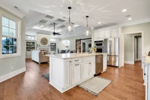 Modern open-concept kitchen with white cabinets, marble island, stainless appliances, and bright living area.