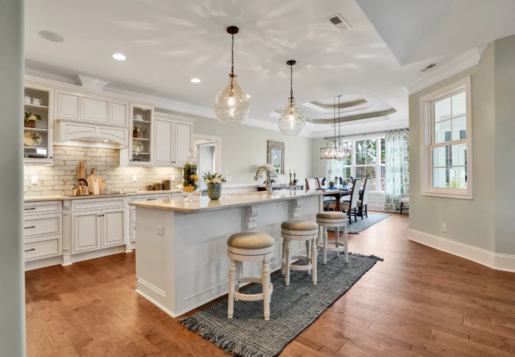 Bright modern white kitchen with large island, wood floors, and open dining area.