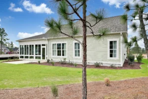 Modern beige single-story house with screened porch, gray roof, and green landscaped yard.