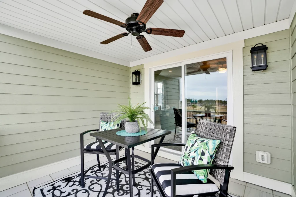 Cozy sage-green balcony with black metal seating, potted plant, ceiling fan, and tropical decor.