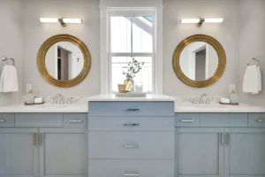 Modern gray-blue double vanity bathroom with gold mirrors, white countertops, and elegant lighting.