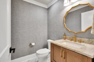Modern gray bathroom with gold accents, marble countertop, and light wood vanity.