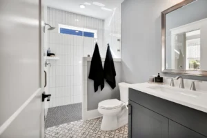 Modern minimalist bathroom with gray vanity, glass walk-in shower, and patterned monochrome tile floor.