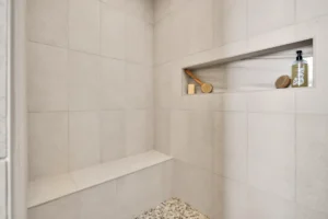 Minimalist modern walk-in shower with tiled bench, recessed shelf, and pebble-style floor.