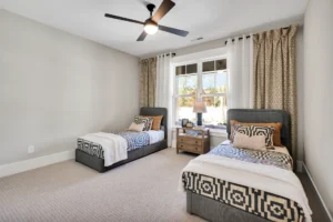 Modern twin bedroom with gray beds, geometric accents, wooden nightstand, and natural light.