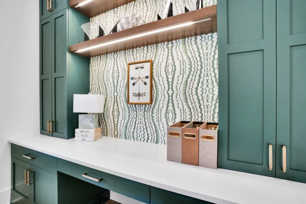 Modern green built-in home office with white countertop, brass accents, and stylish wood shelving.