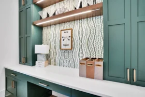 Modern green built-in home office with white countertop, brass accents, and stylish wood shelving.