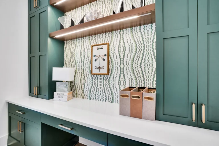 Modern green built-in home office with white countertop, brass accents, and stylish wood shelving.