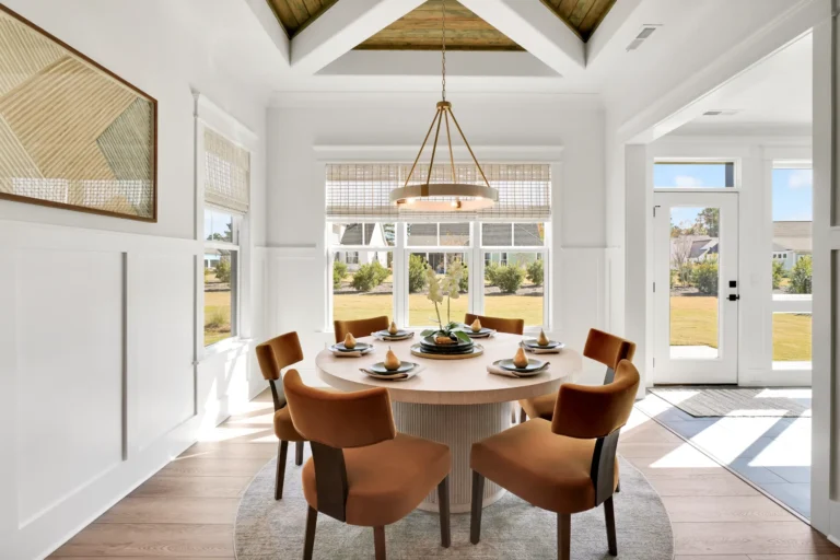 Bright modern rustic dining room with round wooden table, rust chairs, and natural light.