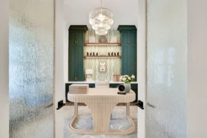 Modern entryway with sculptural wood table, green cabinetry, and cascading glass chandelier.