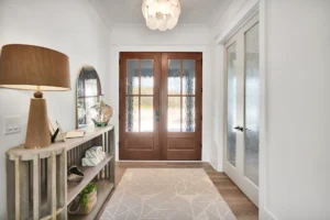Bright modern coastal entryway with glass wooden doors, rustic console table, and shell pendant light.