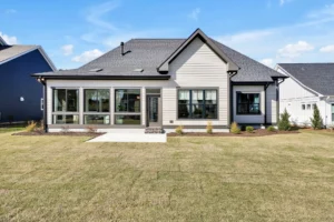 Modern single-story suburban home with gray siding, large windows, patio, and green backyard lawn