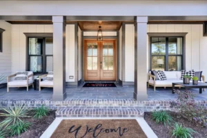 Inviting modern farmhouse porch with wooden double doors, lantern light, cozy seating, and greenery.