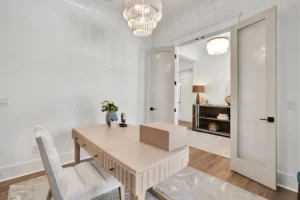 Modern minimalist home office with light wood desk, crystal chandelier, and bright neutral decor.
