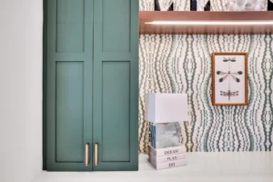 Sage green cabinets with patterned wallpaper and dragonfly art in a modern eclectic interior.