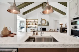 Modern kitchen with white marble island, copper pendant lights, and rustic wood beams.