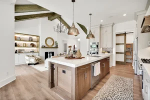 Modern rustic open-concept kitchen with white island, wood beams, and cozy fireplace.