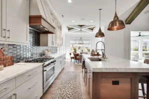 Bright modern kitchen with white marble island, copper lighting, and natural wood accents.