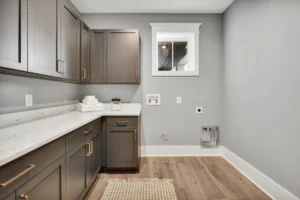 Modern gray laundry room with gold hardware, wood floors, and white countertop.