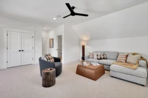 Bright modern living room with gray sectional sofa, tan ottoman, and black ceiling fan.