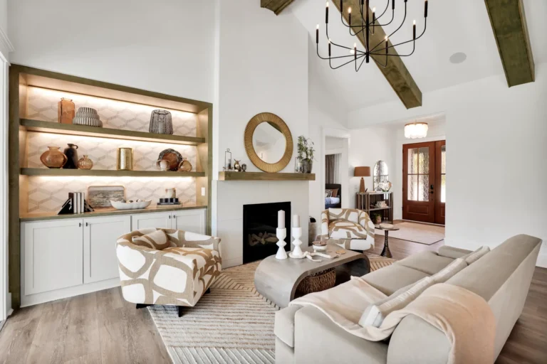 Bright modern farmhouse living room with white fireplace, gold mirror, wood beams, and beige seating.