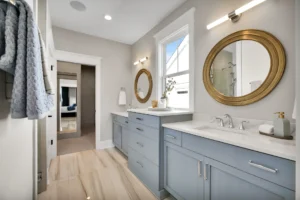 Modern double vanity bathroom with blue cabinets, gold mirrors, and bright elegant lighting.