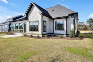 Modern gray house with dark trim, large windows, and landscaped lawn under bright blue sky.