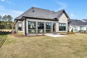 Modern suburban home with large glass windows, patio, and spacious green backyard.