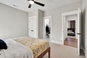 Modern minimalist bedroom with gray walls, wooden bed, gold accents, and sleek black ceiling fan.