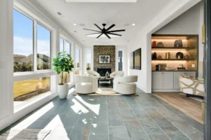Bright modern sunroom with stone fireplace, white chairs, and large windows filled with natural light.