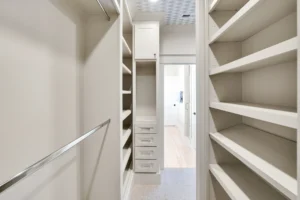 Bright modern white walk-in closet with shelves, drawers, and light wood flooring.
