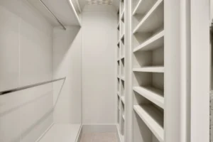 Modern white walk-in closet with double hanging rods, built-in shelving, and soft ambient lighting.