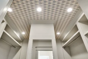 Modern walk-in closet with white shelving, geometric ceiling pattern, and bright recessed lighting.