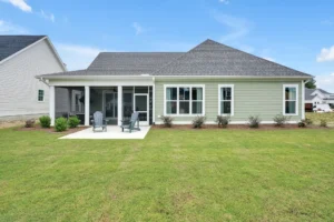 Modern green suburban house with patio, screened porch, and sunny landscaped backyard lawn.
