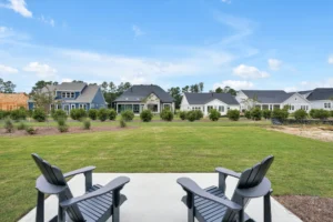 Adirondack chairs on sunny suburban patio overlooking green lawn and modern neighborhood homes.