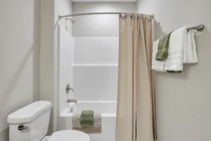 Modern neutral bathroom with white tub, beige shower curtain, and green accent towels.