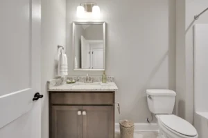 Modern gray bathroom with wood vanity, granite countertop, and warm contemporary lighting.