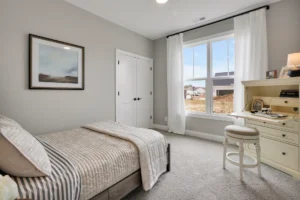 Cozy gray and beige bedroom with sunlight, soft bedding, and a white desk by the window.