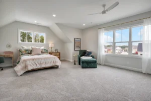 Bright modern bedroom with neutral decor, pastel bedding, and a cozy green accent chair.