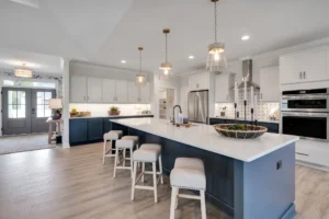 Bright modern kitchen with navy island, white cabinets, stainless steel appliances, and pendant lighting.